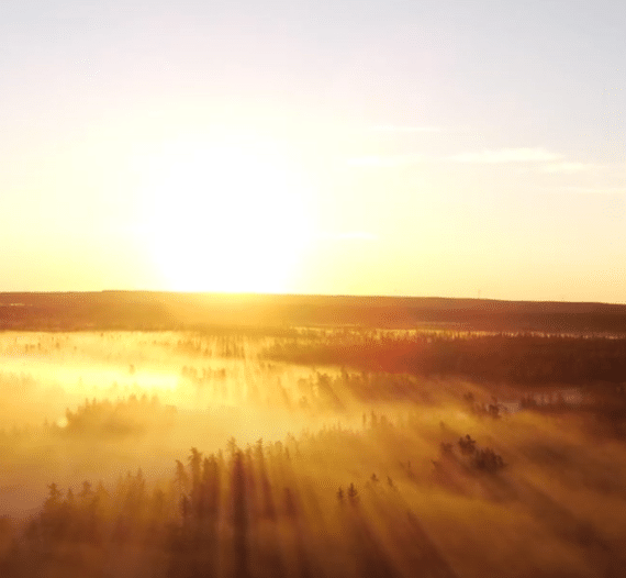 Sunrise is significant on Summer Solstice - the photo shows a sun on a misty landscape along a conifer-covered road and, on the distant horizon, the hillsides. The photo reads: Bonne Journée nationale des peuples autochtones! Happy National Indigenous Peoples Day.