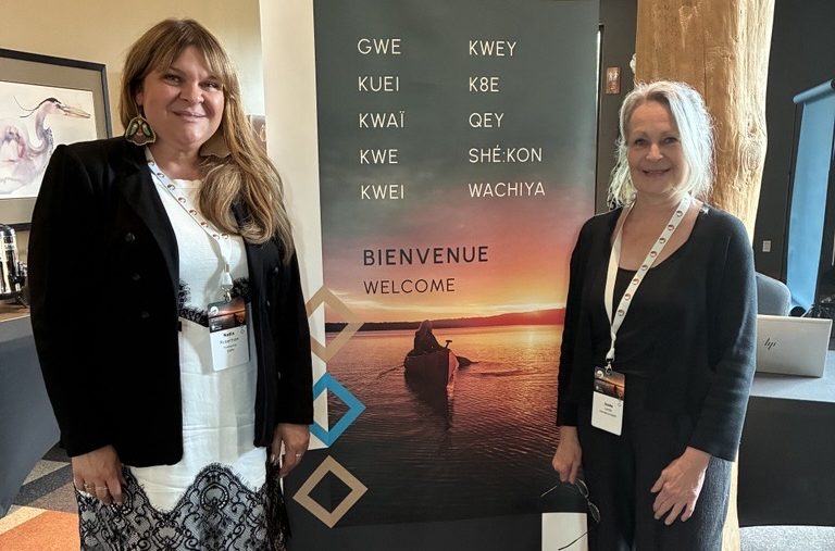 Image (3) Two participants in front of a multilingual welcome banner from the First Nations Executive Education program.