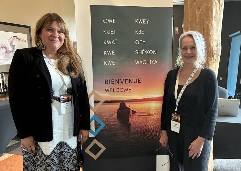 Image (3) Deux participantes devant une bannière de bienvenue multilingue de l’École des dirigeant·e·s des Premières Nations.